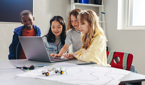 Kids working together to program a robot car with a laptop in a computer science class