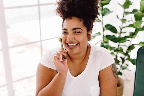 Healthy woman applying massage roller on face