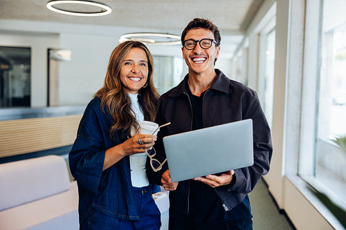 Businesswoman and man share a laptop in office hallway
