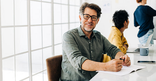 Happy business man sitting in a boardroom. Senior man attending a meeting in an office