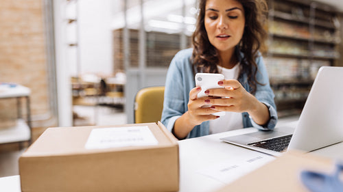 Female online store manager using a smartphone in a warehouse