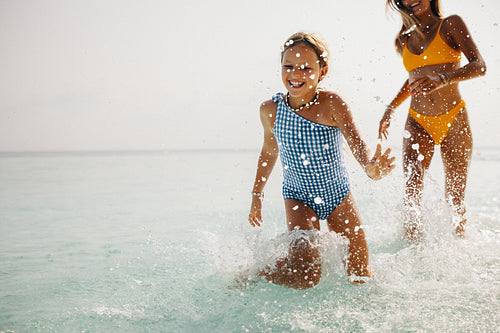 Holiday joy: Girl splashing in the ocean with mother in the background