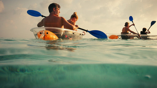 Couple and friends enjoying clear kayaking in tropical waters at stunning sunset or sunrise