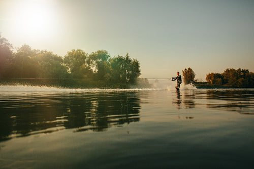 Man wakeboarding on lake at sunset