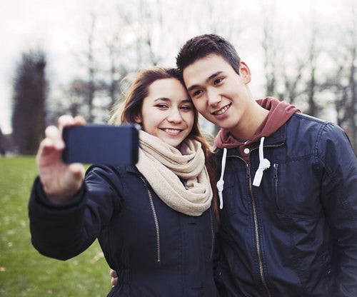 Cute young couple taking self portrait with smartphone in park