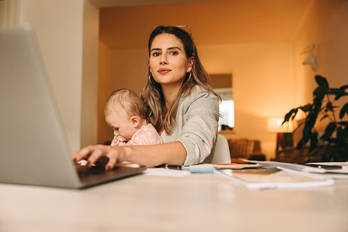 New mother typing on a laptop while working in her home office