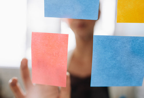 Businesswoman pointing at sticky note on glass wall 