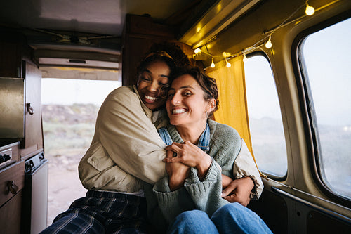 Friends hug inside a cozy camper smiling warmly