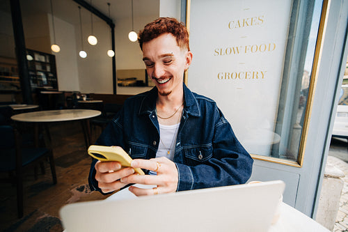 Young man in cafe using smartphone, smiling