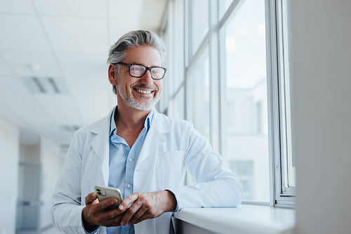 Happy senior doctor holding a mobile phone in a hospital