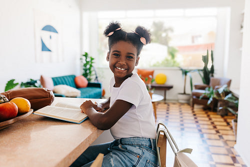 Confident afro-haired black girl practicing reading skills at home