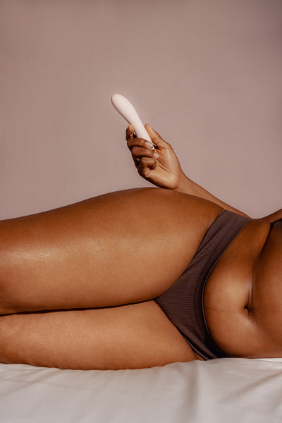 Young woman lying on a bed in underwear, getting ready to play with a feminine adult toy