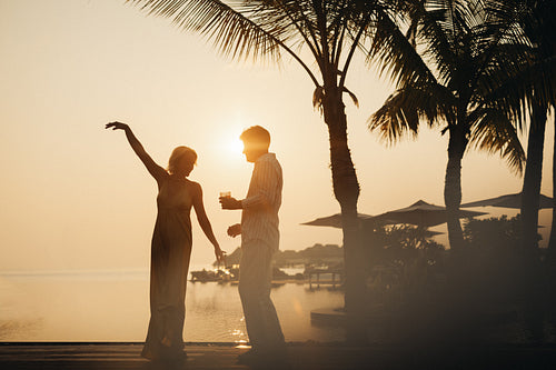 Silhouette of a couple dancing at a sunset holiday resort outdoors with palm trees