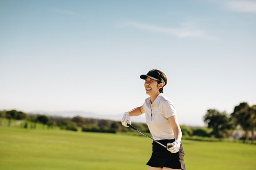 Happy female golfer enjoying a sunny day on the course holding golf club under clear blue skies