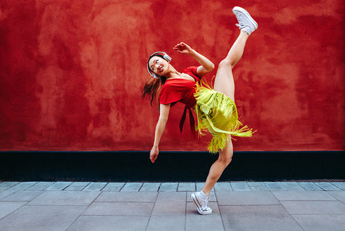 Dance moves carry woman with headphones past a red wall outdoors
