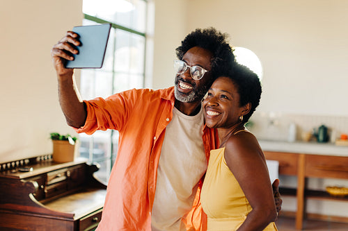 Happy mature couple smiling and taking selfie at home with tablet