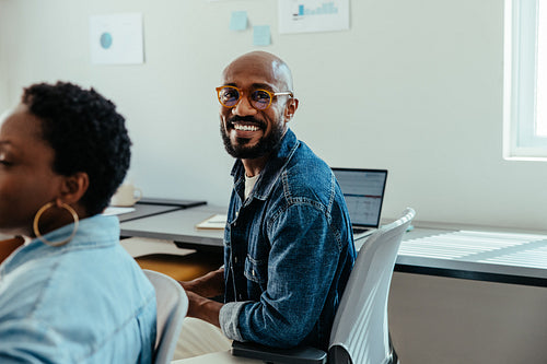 Happy employee smiling in modern office, wearing glasses and denim jacket
