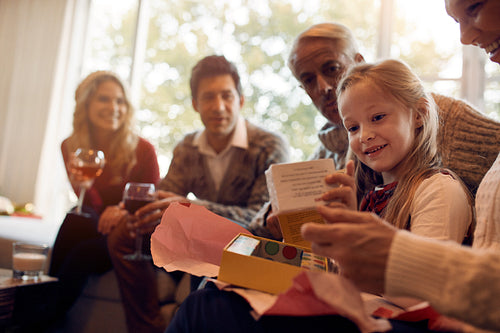 Little girl sitting with family and opening present