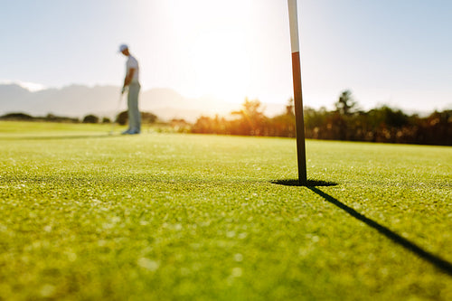 Golf hole and flag in the green field with golfer