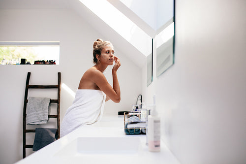 Young woman applying cream on her face in bathroom