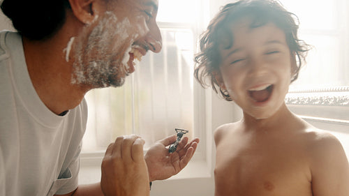 Fun and laughter as a father teaches his son how to shave facial hair at home