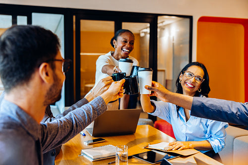 A cheerful group of professionals toasting with coffee in a bright office setting