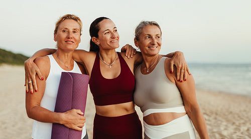Three women embracing on a beach after a yoga session at sunset