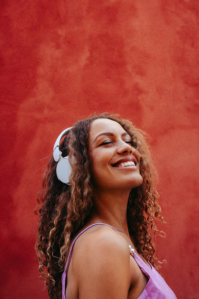 Woman listens to music on headphones in a studio portrait against a red background