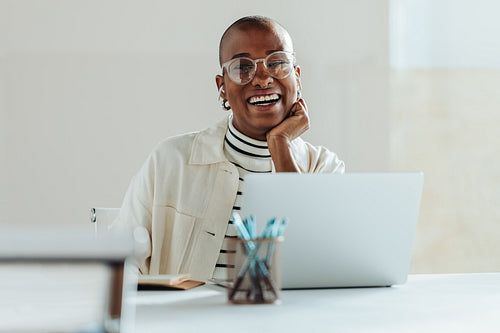 Happy young woman working on a laptop in bright office, expressing success and positivity