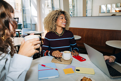 Friends laughing over coffee and working in cafe