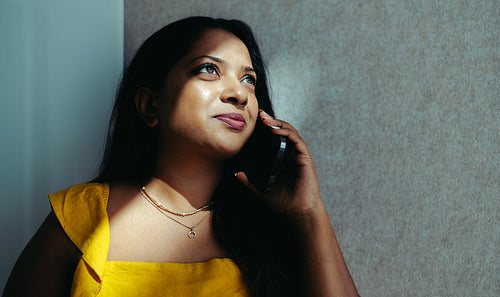 Indian businesswoman on a phone call while standing by a softly lit wall