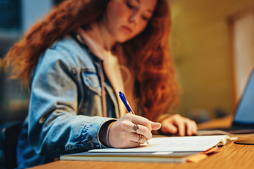 Young student writing notes at library desk