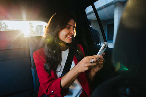 Smiling woman in red blazer using smartphone inside a car