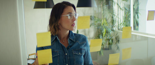 Businesswoman uses sticky notes for planning on glass office wall