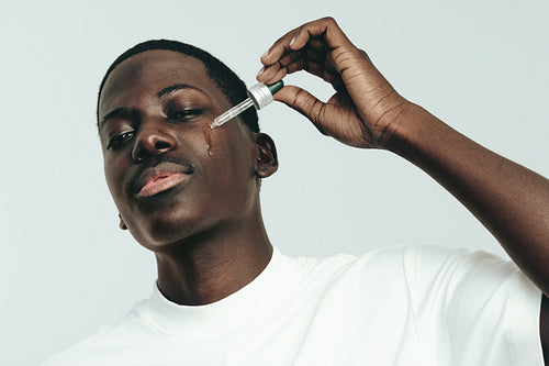 Caring for melanin skin, a young man applies beauty serum to his face