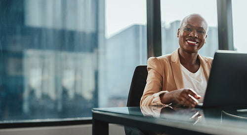 Successful african businesswoman smiling and working on laptop in office