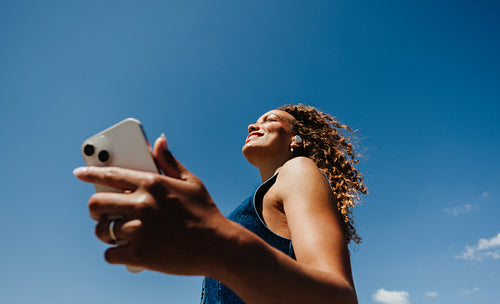 Woman uses smartphone outdoors under a clear blue sky