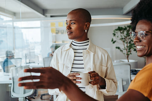 Two business women standing in a modern office, discussing ideas and collaborating on a project