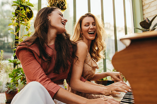 Two cheerful female friends singing and playing the piano