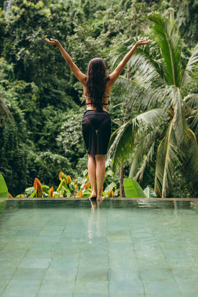 Woman in bikini on the edge of the pool with her arms raised
