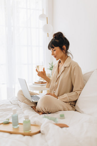 Woman using laptop sitting on bed drinking wine