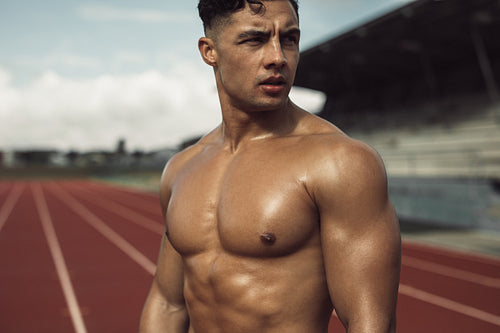 Muscular man relaxing after exercise on track field