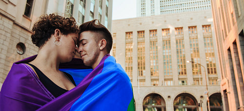 LGBTQ+ couple standing with a rainbow flag around them