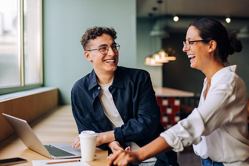 Two young professionals laughing during a casual conversation in the office