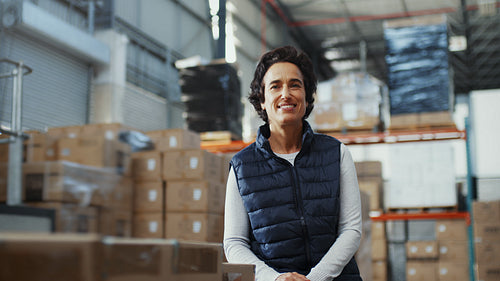 Female warehouse worker smiles at the camera while standing next to boxes of inventory in a warehouse