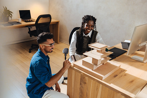 Two young architects discussing a building model in a modern office setting