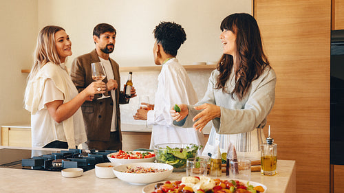 Group of friends enjoying drinks and food during home dinner preparation