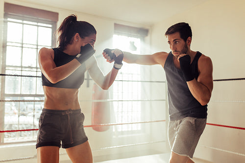 Male fighter with beard striking a female athlete in a boxing ring
