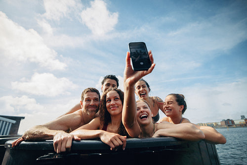 A vacation selfie captures friends relaxing in an outdoor hot tub by the water.