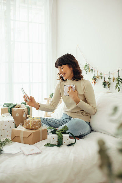 Woman sitting on bed with christmas presents doing a video call